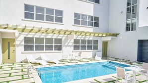 A modern outdoor pool area with a rectangular pool, white lounge chairs, and a pergola structure. - Coral Beach #204 - by ZenBreak (Little Battaleys)