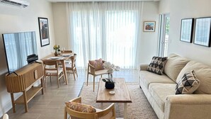 A living room with a sofa, coffee table, dining table, chairs, and a television. - Coral Beach #204 - by ZenBreak (Little Battaleys)