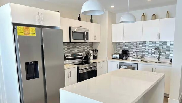 A modern kitchen with stainless steel appliances, white cabinetry, and a central island. - Coral Beach #204 - by ZenBreak (Little Battaleys)