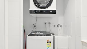 A compact laundry area with a front-loading washing machine, a dryer, and a sink. - MetaWise 1Bed Next Darling Harbour 115 (Sydney)