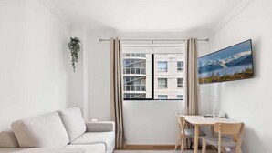 A minimalist room with a white sofa, a small table with chairs, a window with curtains, a plant, and a framed picture on the wall. - MetaWise 1Bed Next Darling Harbour 115 (Sydney)