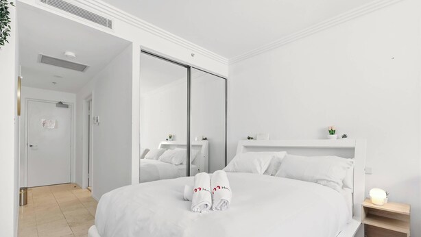 A hotel room with a large bed, a wardrobe with a mirror, a bedside table with a lamp, and a small plant on the nightstand. - MetaWise 1Bed Next Darling Harbour 115 (Sydney)