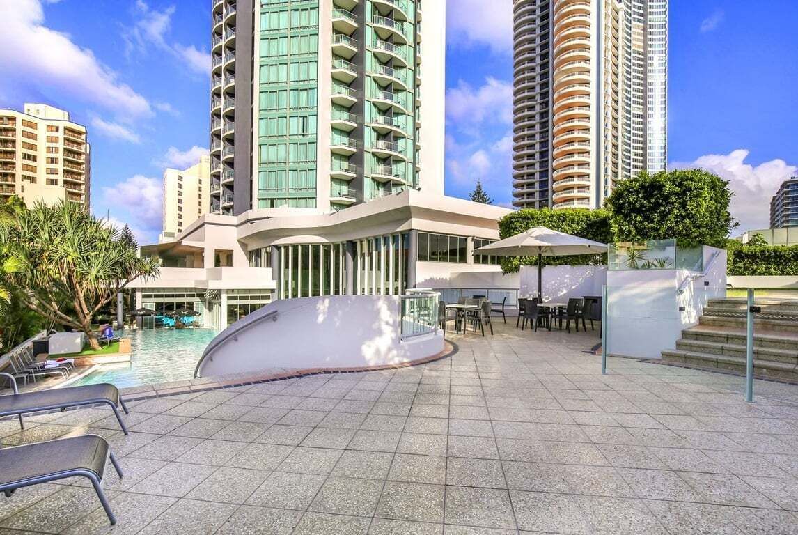 A hotel with a swimming pool, outdoor seating, and high-rise buildings in the background.