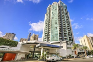 Un hôtel de grande hauteur au design moderne, doté d’une entrée imposante et d’un espace de stationnement bien visible.