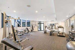 Une salle de sport moderne équipée de divers appareils d’exercice, dotée de grandes fenêtres et d’un sol recouvert de moquette.