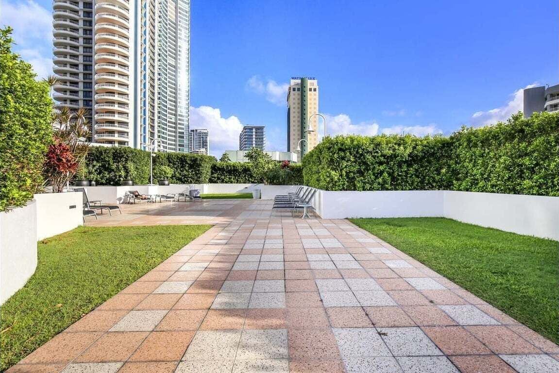 Un chemin menant à un bâtiment à l’architecture moderne, entouré de verdure et sous un ciel dégagé.