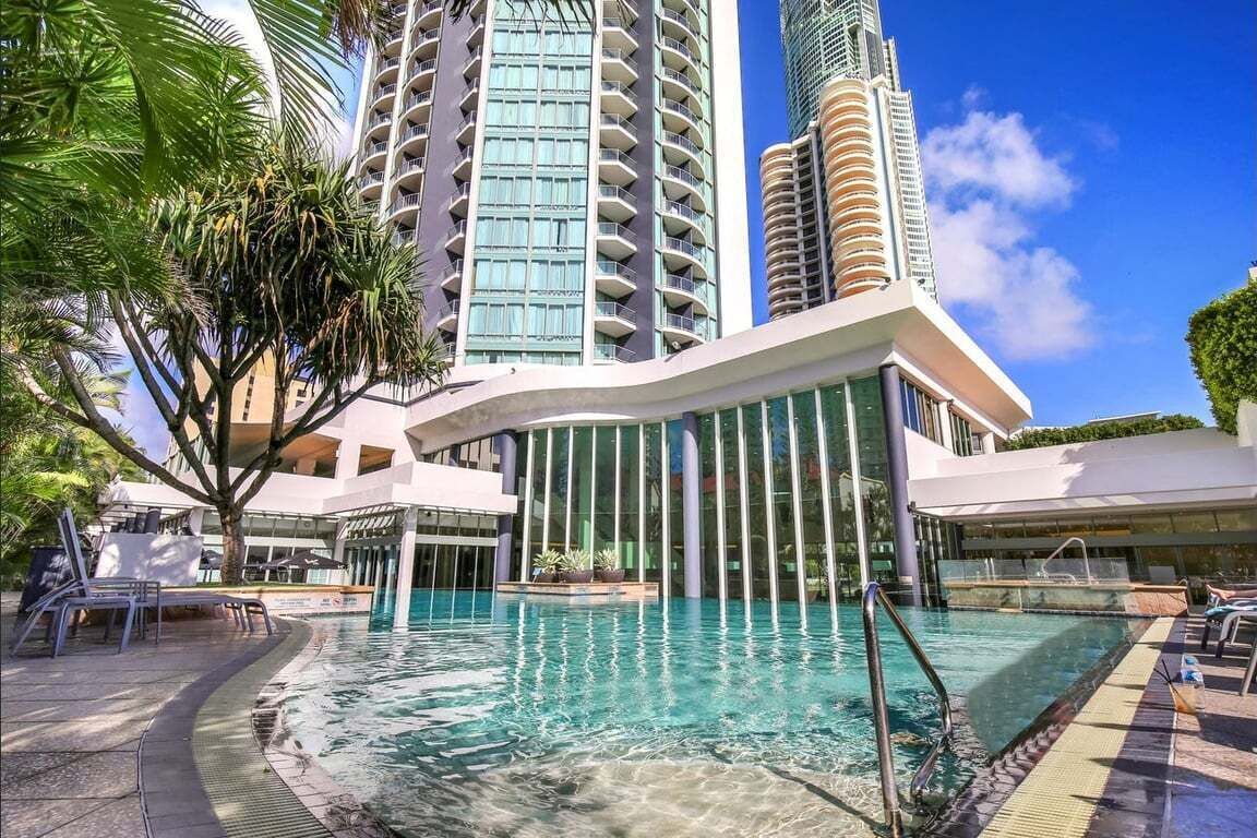 A hotel with a swimming pool, modern architecture, and high-rise buildings in the background.