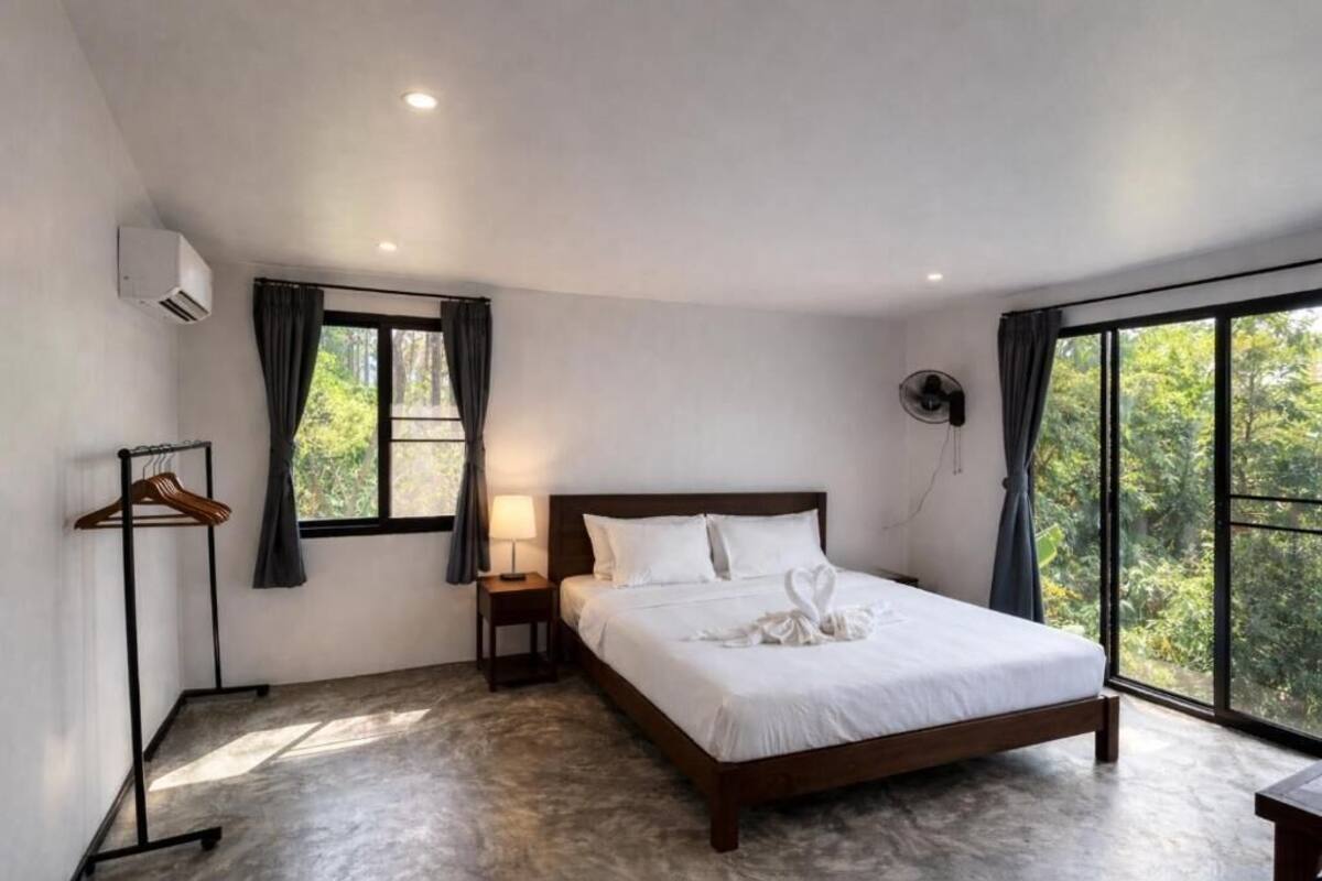 A bedroom with a bed, a nightstand, a wall-mounted fan, and a window with curtains.