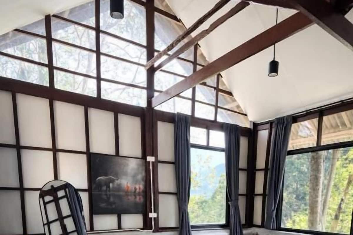 A room with a bed, a large window, a stone wall, and a hanging light fixture.