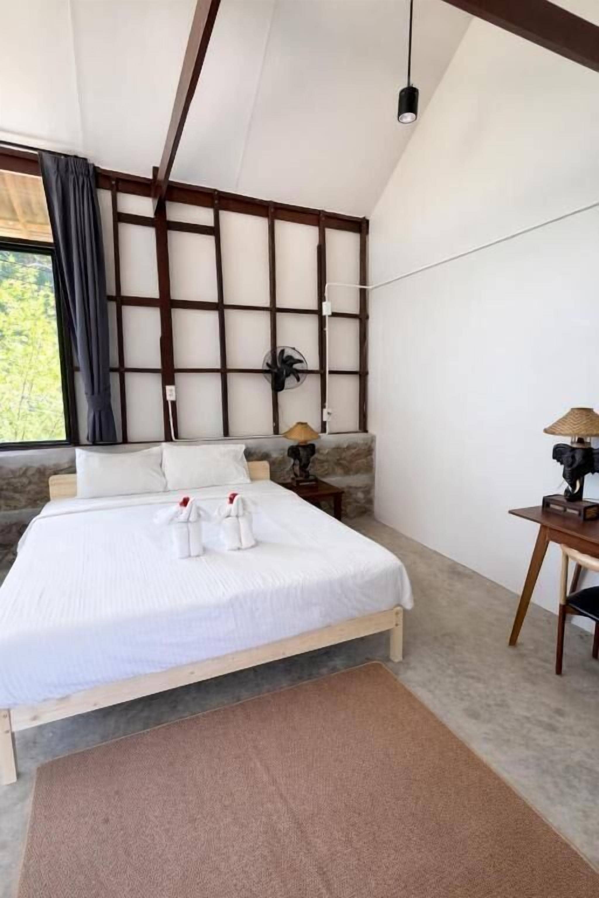 Un dormitorio con cama, mesita de noche, lámpara y vistas al exterior.
