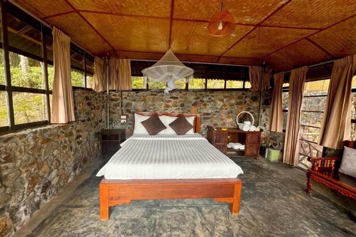 A room with a stone wall, a wooden bed, a hanging light fixture, and a window with curtains.