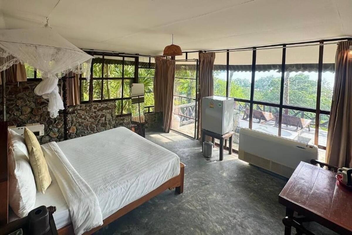 A bedroom with a bed, a desk, a chair, a TV, and a view of the outdoors.