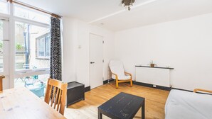 Une pièce avec un plancher en bois, une chaise blanche, une table noire, un radiateur et une fenêtre avec un rideau.