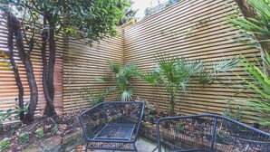 Un jardin avec une clôture en bois, deux chaises en métal et une variété de plantes.