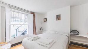 Une chambre à coucher avec un grand lit, une fenêtre donnant sur un immeuble, une table de chevet et une chaise.
