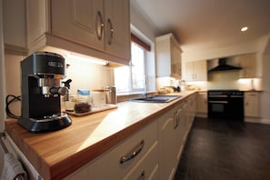 A modern kitchen with a coffee maker, wooden countertop, and white cabinets. - Delightful 5-bedroom detached house in charming Frome perfect for long stays (Frome)