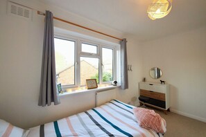 A bedroom with a bed, a dresser, a window with curtains, a radiator, and a wall-mounted mirror. - Delightful 5-bedroom detached house in charming Frome perfect for long stays (Frome)