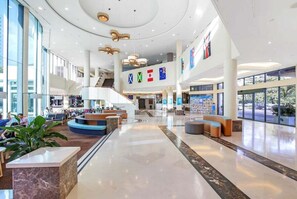 Eine großzügige Lobby mit einer zentralen Treppe, Sitzbereichen und einer Rezeption.