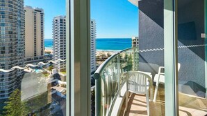 A balcony with a view of the ocean and beach, a glass railing, and a white chair. - Skyline Stay with Balcony (Gold Coast)