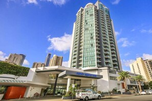 Ein hoch aufragendes Hotel mit modernem Design, das eine markante Eingangsfront und einen sichtbaren Parkbereich aufweist.