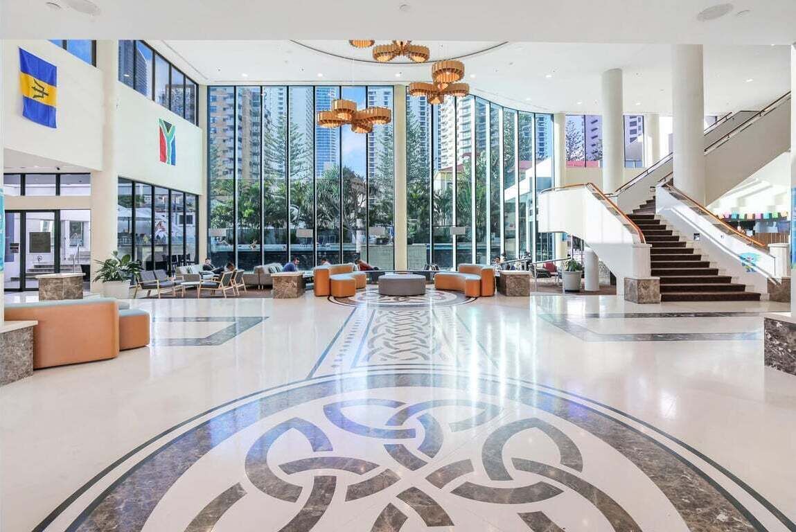 Eine geräumige Lobby mit einer zentralen Sitzgelegenheit, einer Treppe und großen Fenstern mit Blick auf hohe Gebäude.