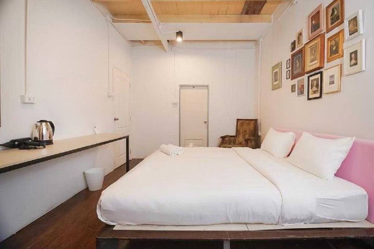 A bedroom with a bed, a desk, a chair, a door, and framed pictures on the wall.