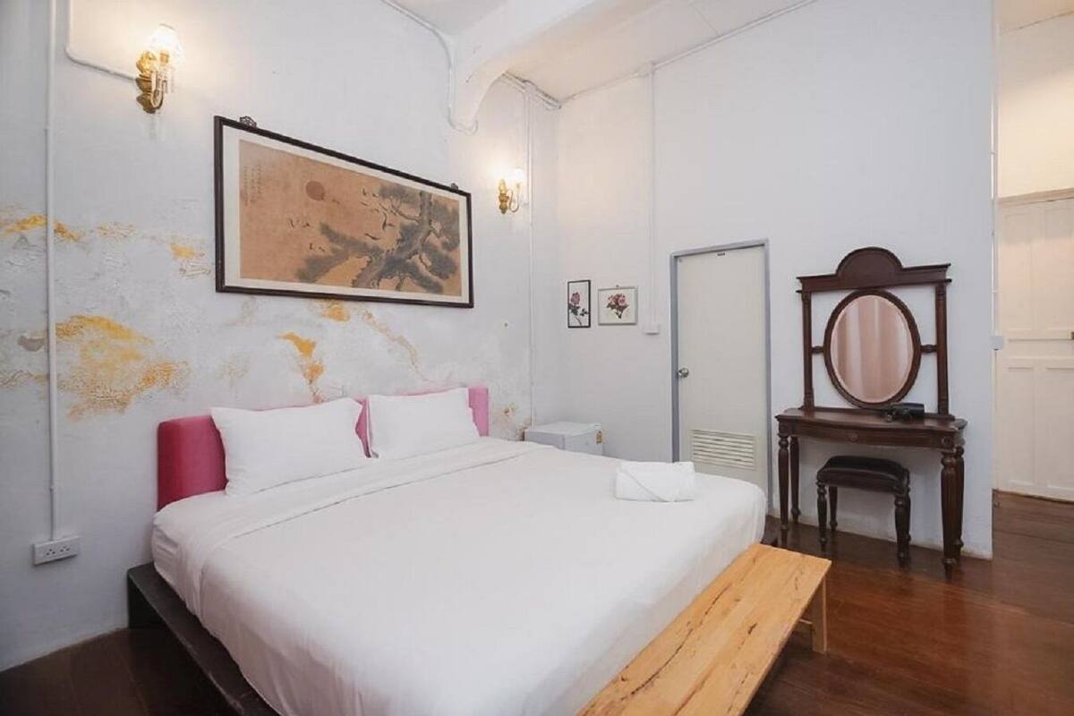 A bedroom with a bed, a wooden bench, a dresser, a mirror, and a painting on the wall.
