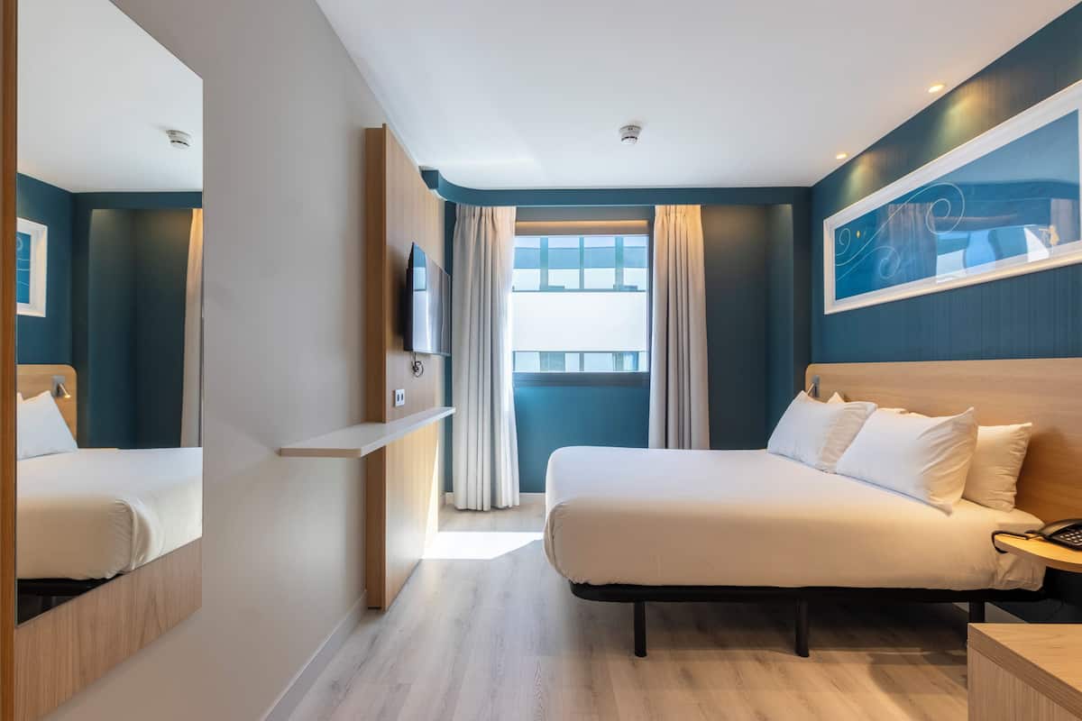 Een hotelkamer met een bed, nachtkastje, televisie en een raam met gordijnen.