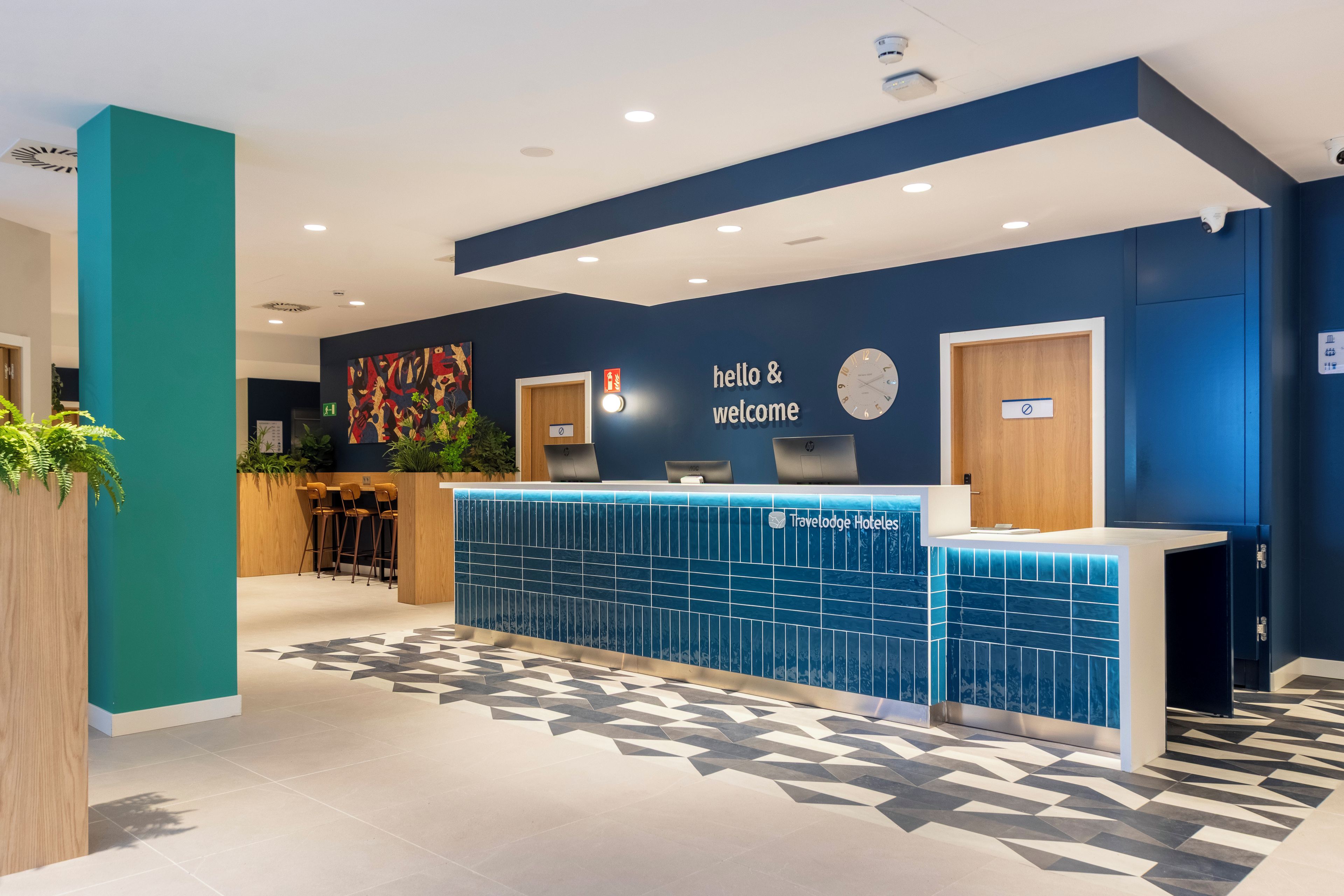 Un mostrador de recepción con un cartel que dice 'hola y bienvenida', un reloj y el logotipo de 'Travelodge Hotels'.