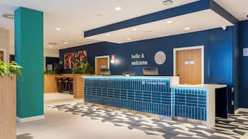 Taulell de recepció amb un cartell de 'hello & welcome', un rellotge i el logotip de 'Travelodge Hotels'.