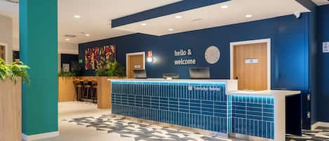 Un mostrador de recepción con un cartel que dice 'hola y bienvenida', un reloj y el logotipo de 'Travelodge Hotels'.