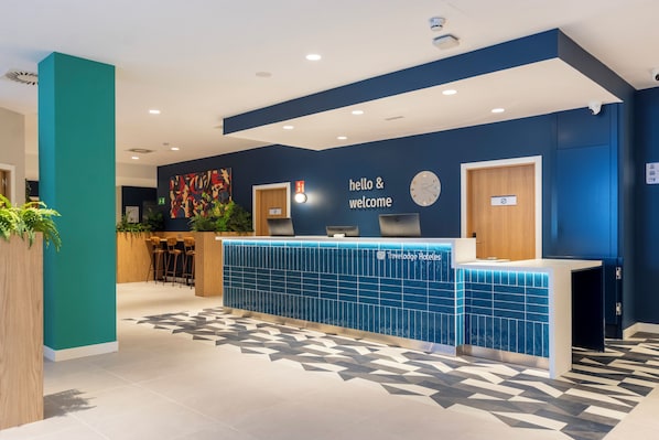 Een receptiebalie met een bord waarop 'hello & welcome' staat, een klok en het logo van 'Travelodge Hotels'.