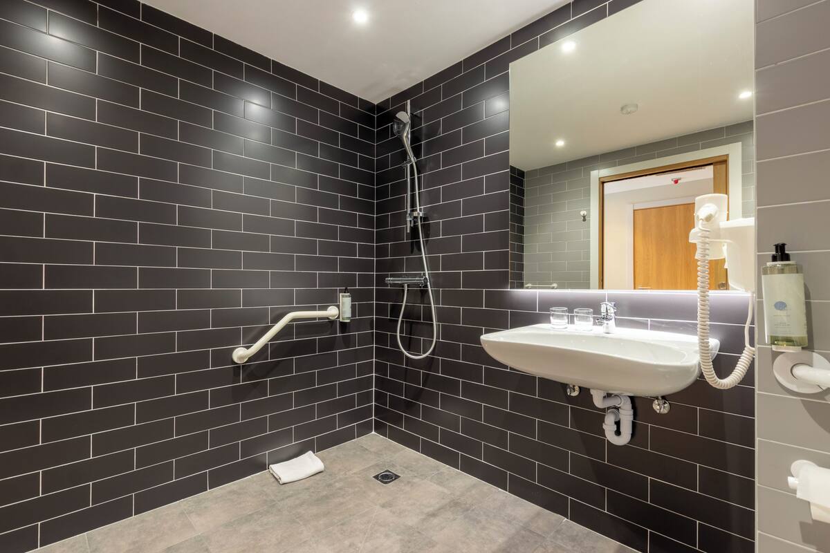 Een moderne badkamer met donkere betegelde wanden, een witte wastafel en een douche.