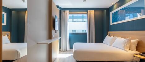 A hotel room with a bed, bedside table, TV, and a window with curtains.