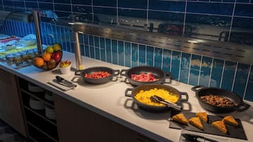 Ein Buffet mit verschiedenen Speisen, darunter Obst, Fleisch und Rühreier, mit einer Fliesenwand und Blick auf einen Pool.