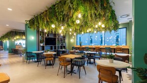Een moderne, overdekte eetruimte met tafels en stoelen, een bar en een plafond versierd met hangende planten en verlichting.