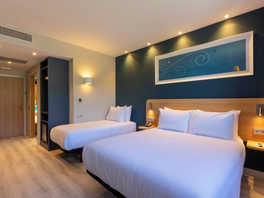 Habitación de hotel con dos camas, un armario de madera, un cuadro en la pared y una mesita con un teléfono.