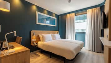 A hotel room with a bed, bedside table, lamp, and a large window with curtains.