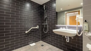 Uma casa de banho moderna com paredes azulejadas escuras, uma pia branca e um chuveiro.