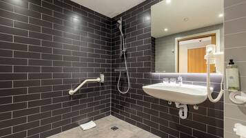 A modern bathroom with dark tiled walls, a white sink, and a shower.