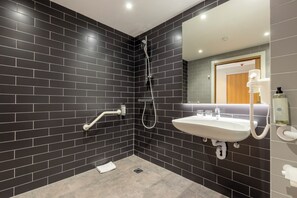 Une salle de bain moderne avec des murs recouverts de carreaux foncés, un lavabo blanc et une douche.