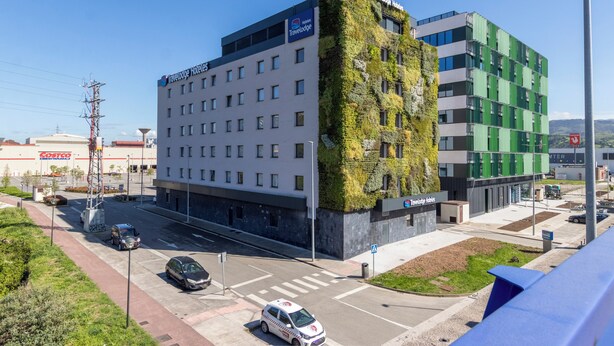 Ein Hotel mit modernem Design, das eine grüne Fassade und mehrere Stockwerke aufweist.
