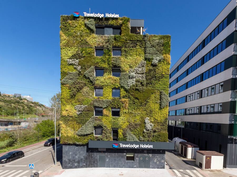 Een modern gebouw met een Travelodge Hotels bord, een groene wand en een heldere lucht.