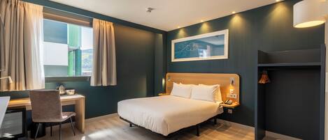 Una habitación de hotel moderna con cama, escritorio, silla y ventana con cortinas.