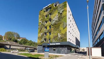 Un edificio moderno con el rótulo de Travelodge Hotels, fachada verde y un área de estacionamiento.