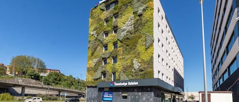 Un edificio moderno con el rótulo de Travelodge Hotels, fachada verde y un área de estacionamiento.