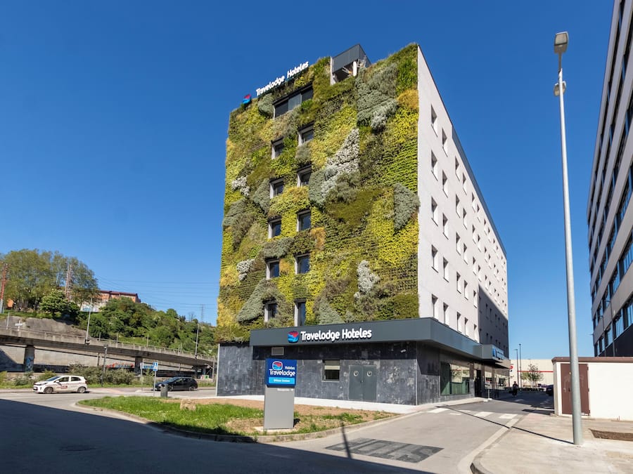 Un edificio moderno con el rótulo de Travelodge Hotels, fachada verde y un área de estacionamiento.