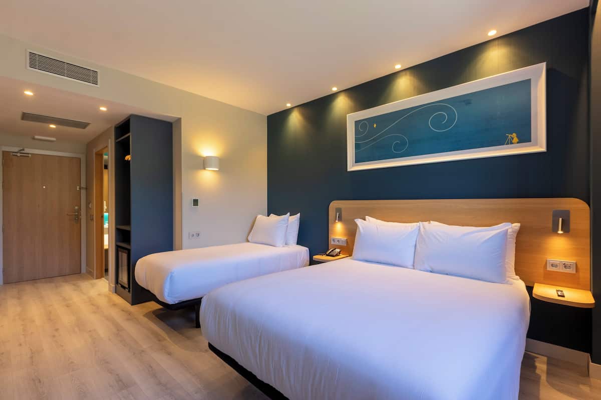 Een hotelkamer met twee bedden, een houten kledingkast, een schilderij aan de muur en een kleine tafel met een telefoon.