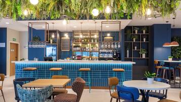 Zona de bar amb taulell blau de rajoles, tamborets i plantes penjants.