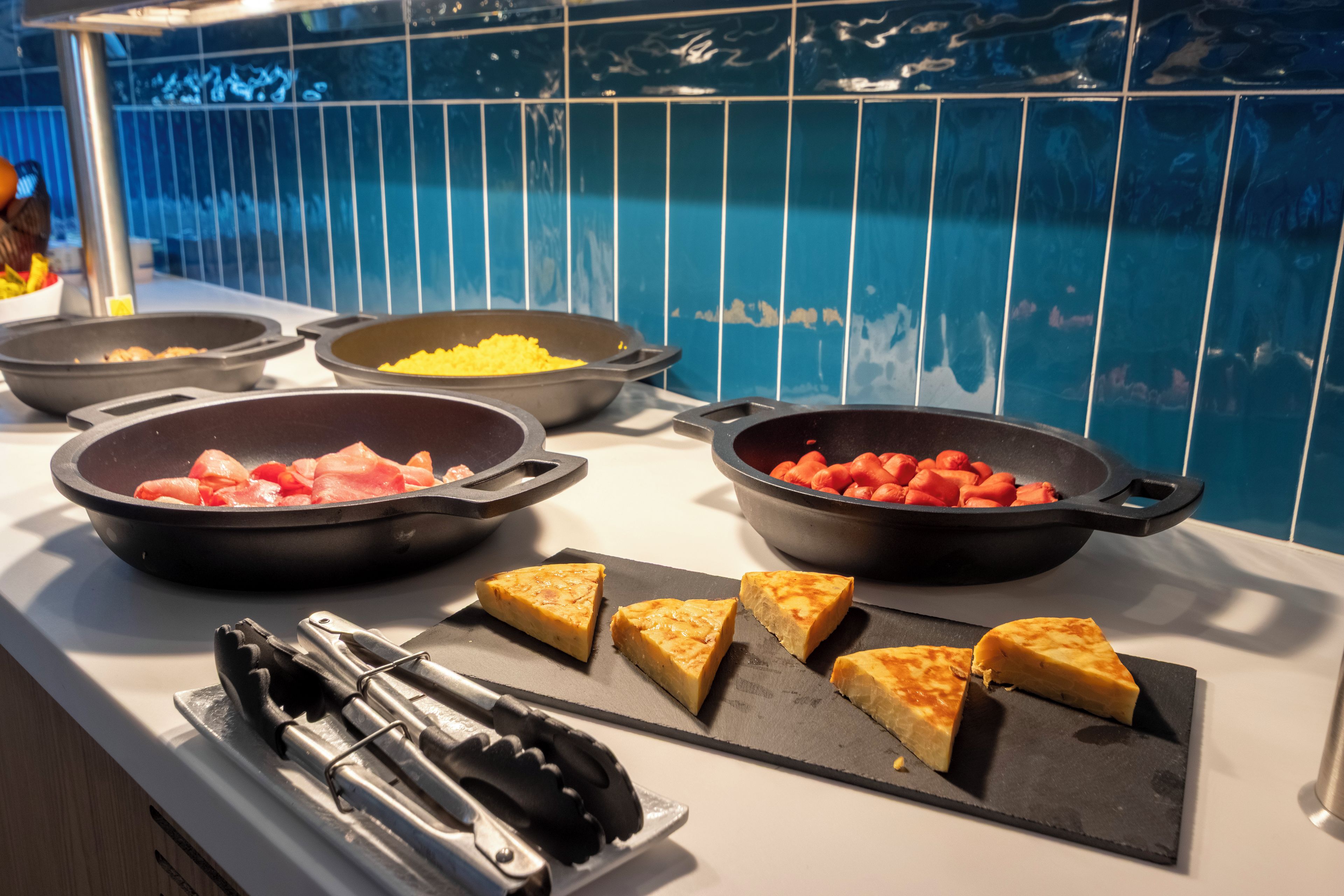 Un buffet proposant une variété de plats, notamment des viandes et des légumes cuits, ainsi qu’un assortiment de pain grillé.